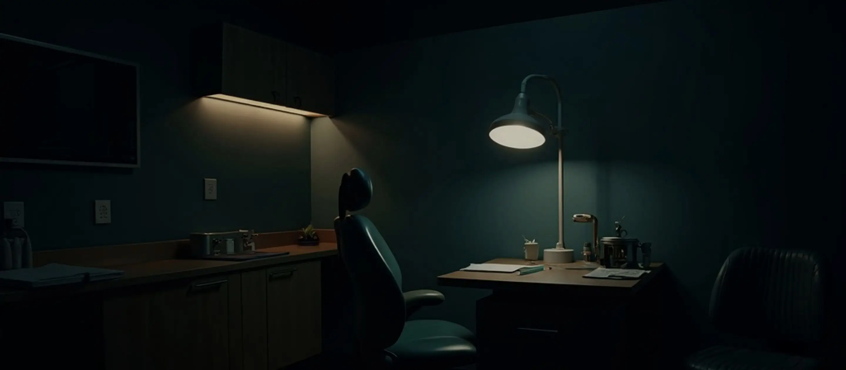 Dental operatory at night, instruments put away, one warm task lamp lighting the counter