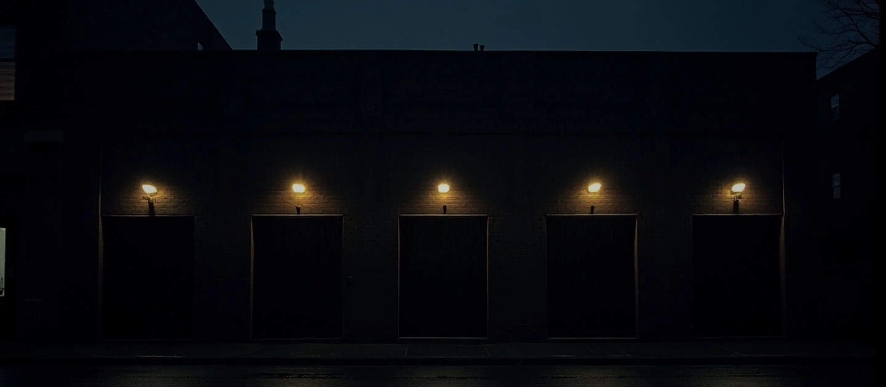 Dark main street at night; above each storefront door a single small warm light is on